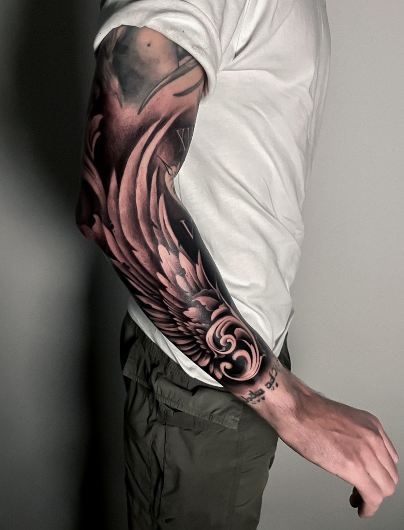 Full sleeve réaliste — ailes d'ange, chiffres romains et volutes baroques en noir et gris