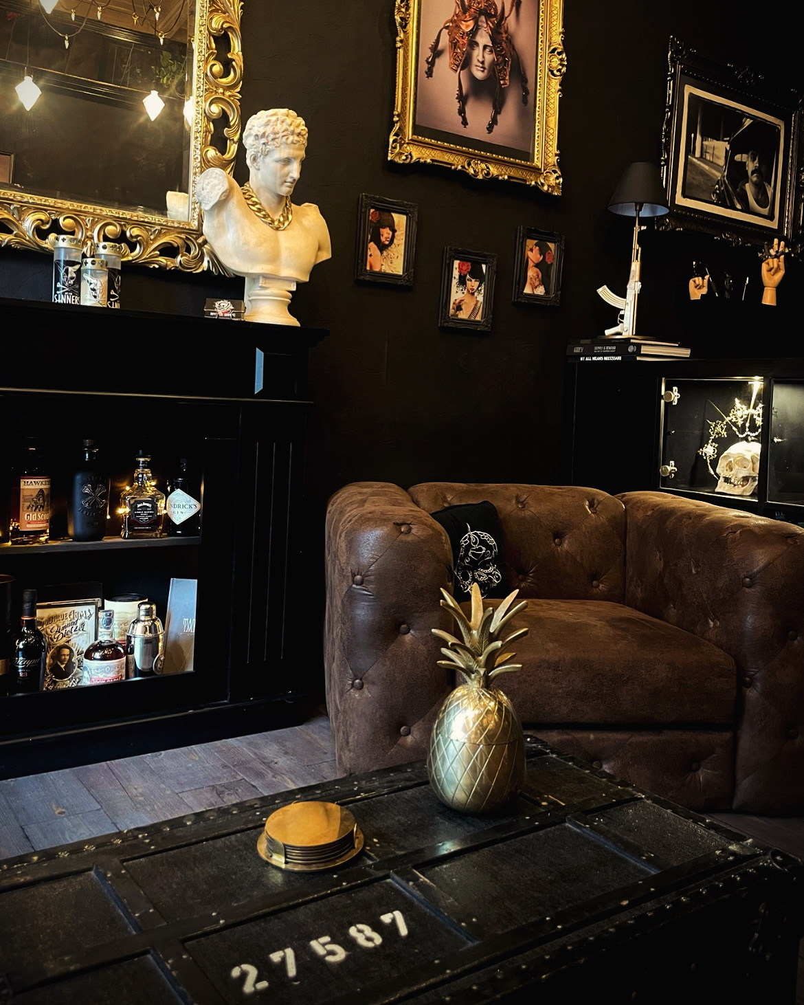 Intérieur du studio Art For Sinners — salon baroque sombre, fauteuil Chesterfield, cadres dorés, buste antique et décoration raffinée