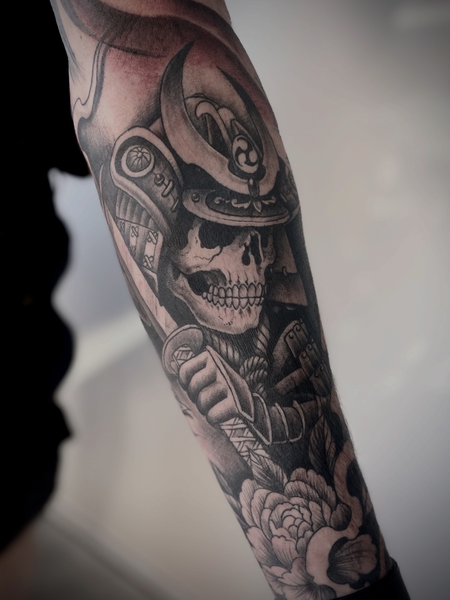 Crâne de samouraï avec katana et pivoines, tatouage noir et gris sur l'avant-bras